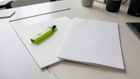 Two overlapping blank pages with a highlighter pen on a clean office desk.